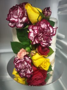 Extra tall cake with buttercream frosting with fresh roses and carnation decorations