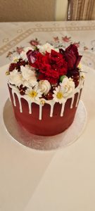Small red celebration cake with white chocolate drip and fresh flowers