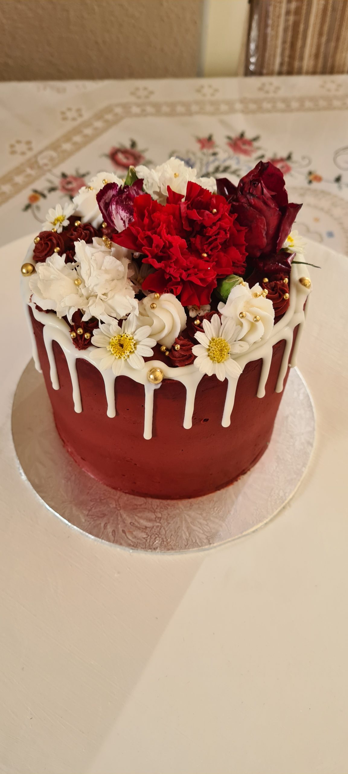 Small red celebration cake with white chocolate drip and fresh flowers